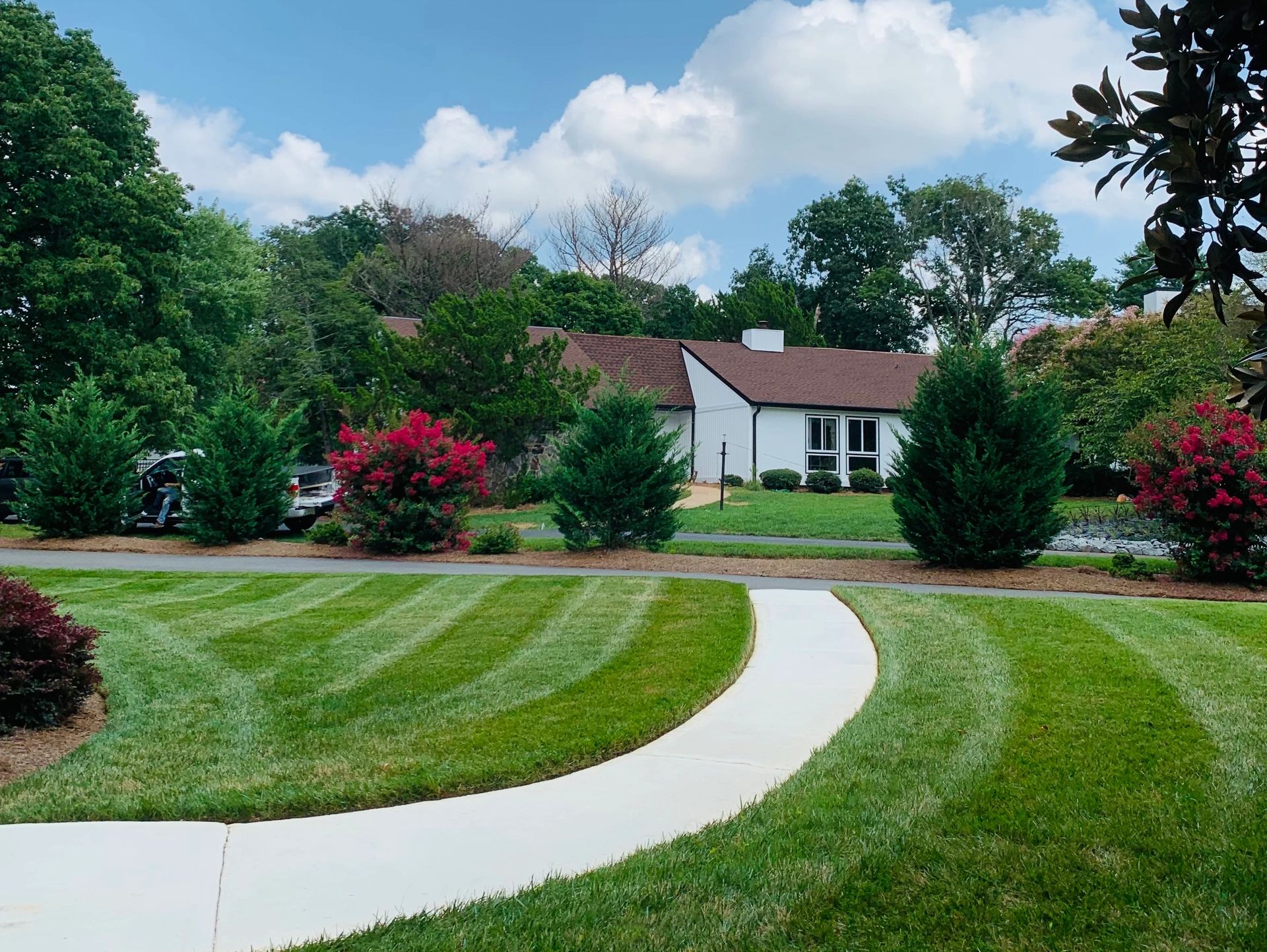 A well-manicured lawn with mowing patterns in front of a white house with black trim and a curved co