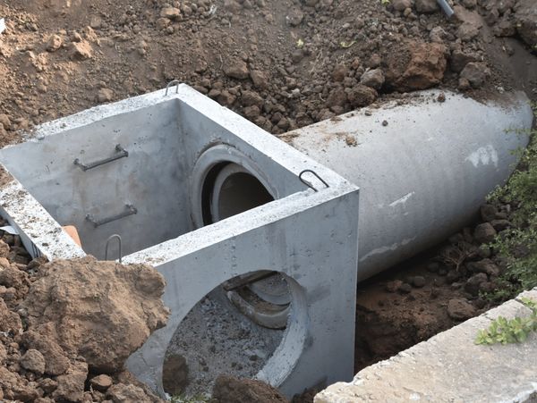 A concrete manhole ring being installed into the ground with a concrete pipe connected to it