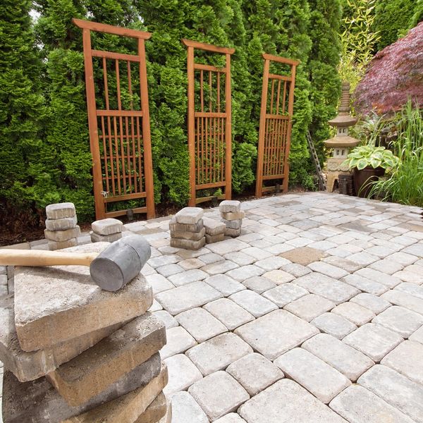 A patio under construction with stacked stone pavers and a rubber mallet leads to a wooden trellis