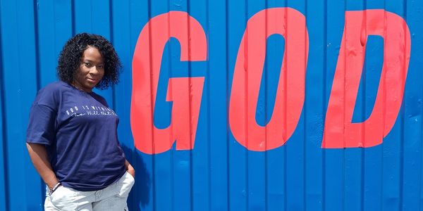 Woman standing by wall with large 'GOD' text.