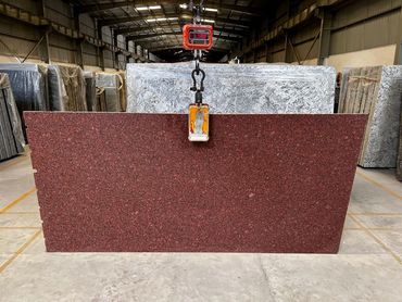 Large red granite slab being lifted in a warehouse.