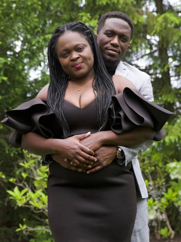 Couple embracing in a lush green outdoor setting, dressed elegantly.