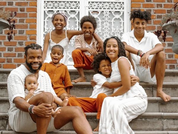 Smiling family of eight sitting on stone steps in front of a brick building.