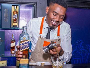 Bartender pouring whiskey with a smile behind the bar.