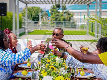 Group of friends toasting with drinks at a sunny outdoor table decorated with flowers and lemons.