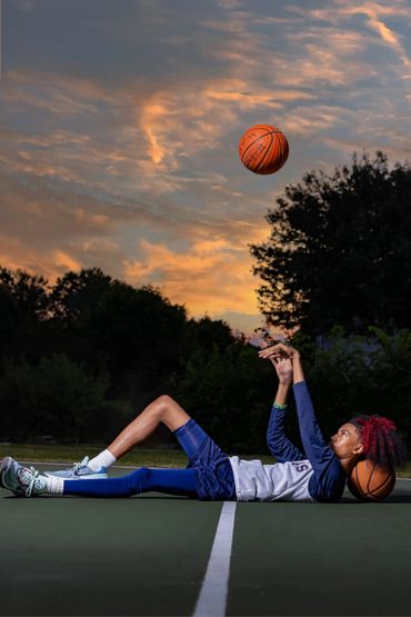 young boy laying on a basketball court throwing ball in the air