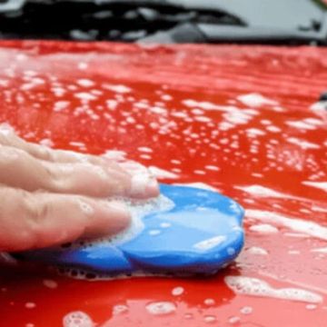 A person washing the hood of a red car