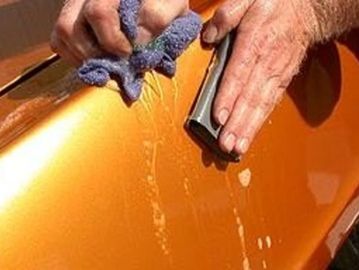 A person washing an orange car