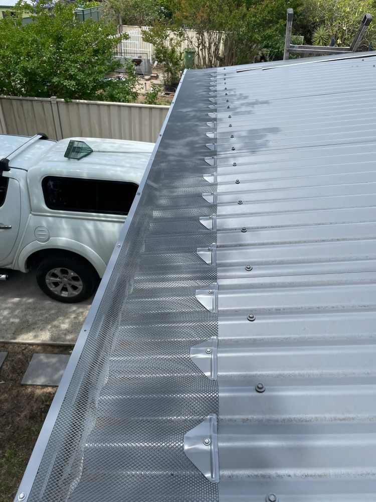 Metal roof with installed mesh gutter guard and a white car in the background.