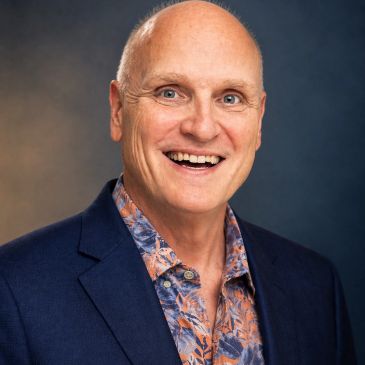 Smiling bald man in a blue blazer and floral shirt.