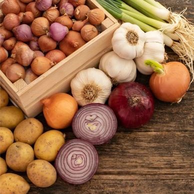Assorted onions, garlic, and potatoes on a wooden surface.
