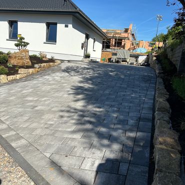 Newly paved driveway beside a modern white house with garden and construction in background.