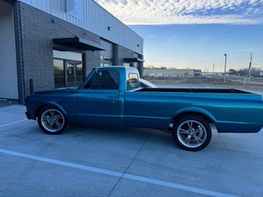 A sleek blue vintage pickup truck parked outside a modern building.