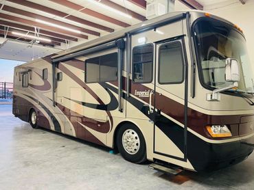 A large beige and brown motorhome named Imperial parked inside a garage.