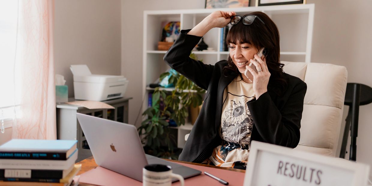 Smiling woman talking on phone at her desk with laptop and books.