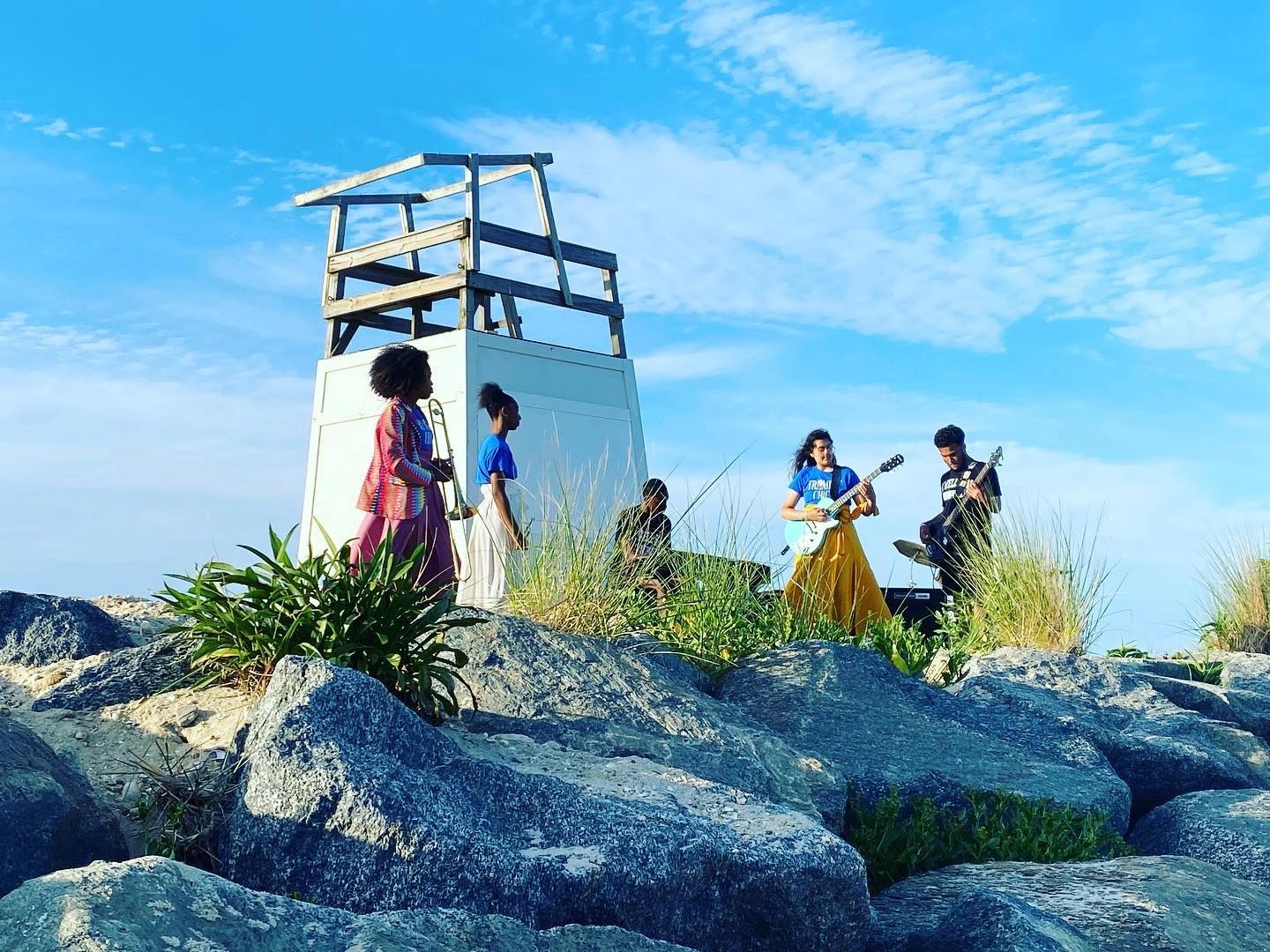 A band plays music outdoors near a lifeguard tower on a sunny day.