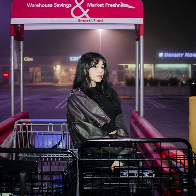 Young woman posing in a shopping cart at night outside a Smart & Final store.