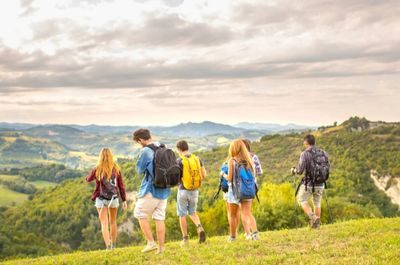 Group of friends hiking on a scenic hillside with backpacks.