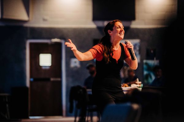 Woman praising God with a microphone in one hand and the other stretched out.