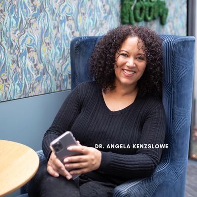 Dr. Angela Kenzslowe sitting on a blue chair smiling.