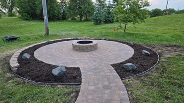Newly built circular brick fire pit with surrounding mulch and stones in a green yard.