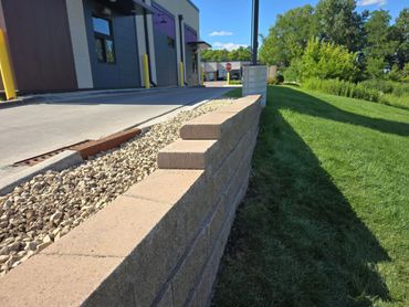 A sunlit retaining wall with gravel and green grass beside a building.