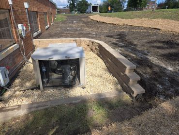 Air conditioning units beside a brick building with a retaining wall and gravel bed.