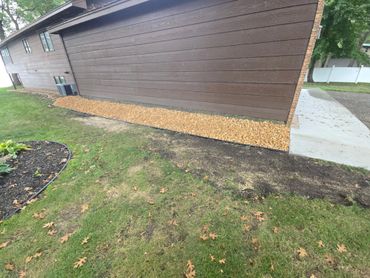 Freshly laid gravel along the brown house wall with a nearby garden bed and lawn.