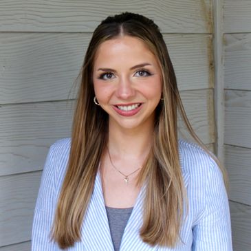 Young woman with long straight hair smiling in front of wooden wall.