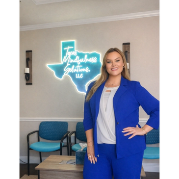 Woman in blue suit standing confidently in an office with Texas Mindfulness Solutions sign.