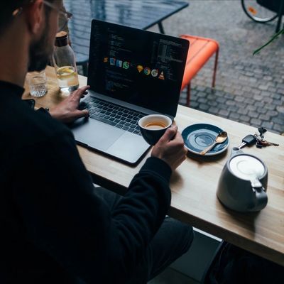 man holds black tea mug while at cafe working at computer tea kettle on desk nearby