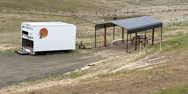 A white trailer and a metal shelter in a dry, fenced rural area.