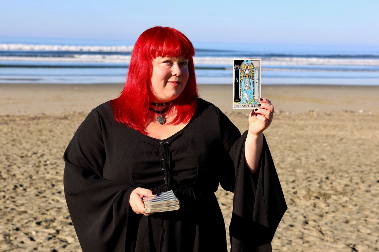 Turning Tides Tarot owner and intuitive reader Alishia Fox on beach holding The High Priestess card