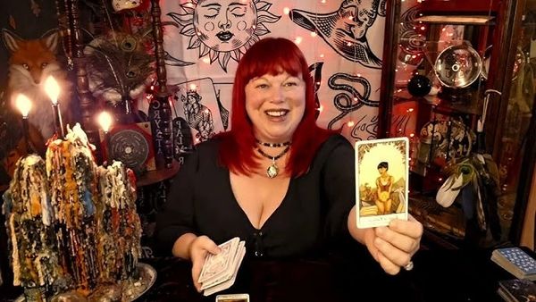 Alishia Fox, Intuitive Reader holding up a tarot card with candles burning beside her during reading