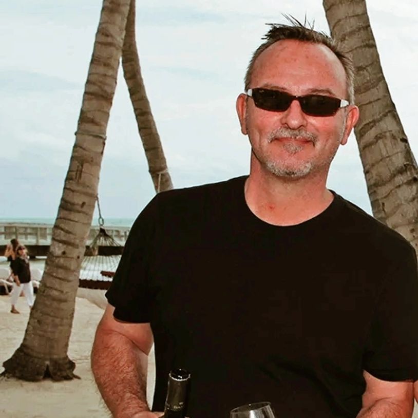 Man in sunglasses holding a drink on a beach with palm trees.