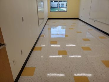 Empty classroom with shiny tiled floor and a window showing outdoor grass area.