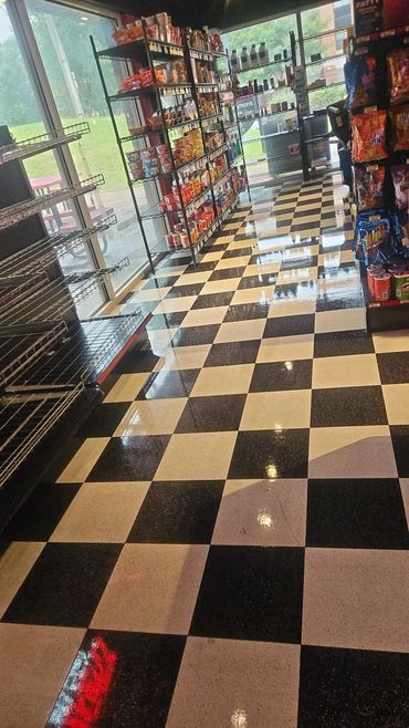 Checkerboard floor and stocked shelves in a small convenience store aisle.