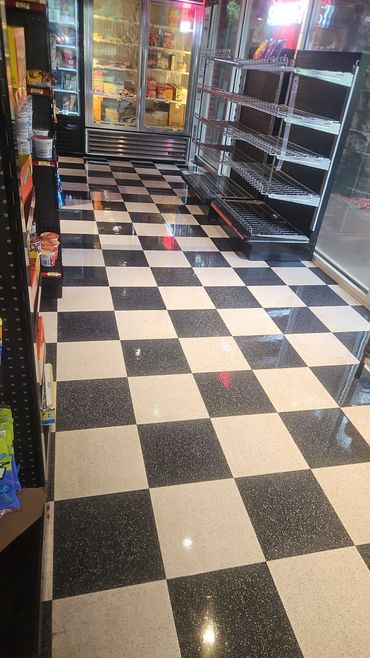 Empty store aisle with black and white checkered floor and refrigerated section.