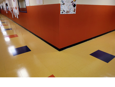 School hallway with colorful tiled floor and student posters on walls.