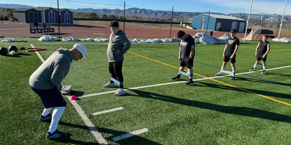 Coach instructs kids doing resistance band exercises on a sports field with mountains in the background.