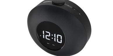 A modern black digital alarm clock showing 12:10.