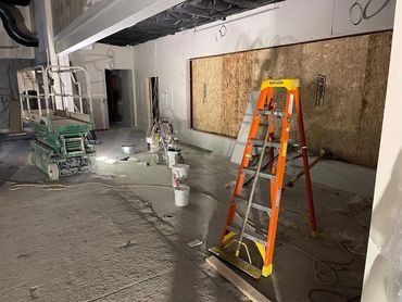 Construction site with ladder, paint buckets, and equipment under dim lighting.