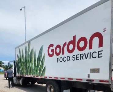 A Gordon Food Service truck parked outdoors with green vegetable graphics.