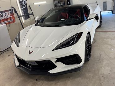 White Chevrolet Corvette parked inside a garage with a black roof and red seats.