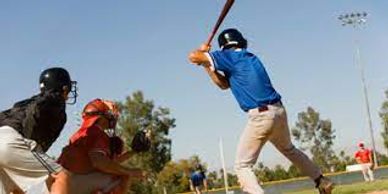 Photo of a softball batter from behind ready to hit a pitched ball with a catcher and umpire in the 