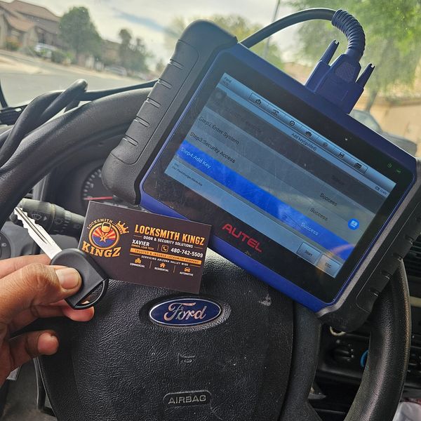 A locksmith holding a key fob and business card inside a Ford vehicle with diagnostic tool.