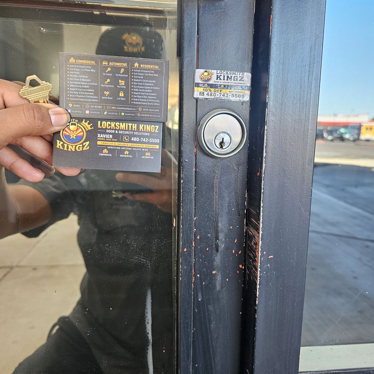 Hand holding Locksmith Kingz business card near a door lock.