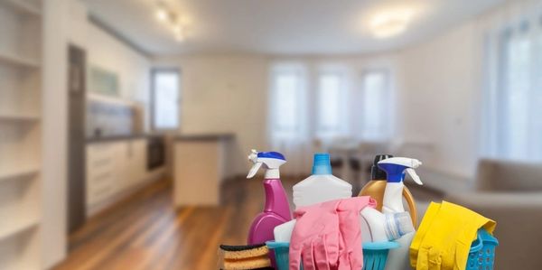 Cleaning supplies including gloves, sprays, and sponges on a table in a modern kitchen.
