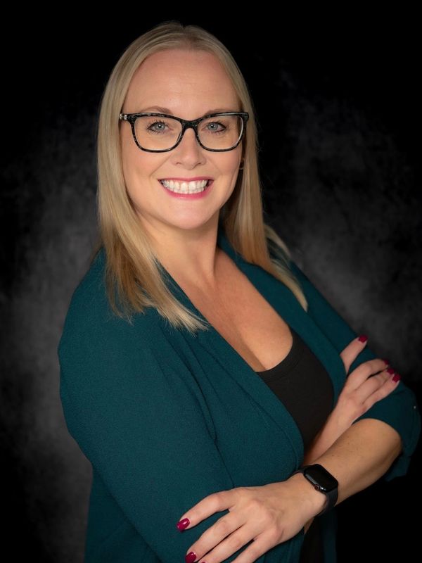 Confident woman with blonde hair and glasses smiling against a dark background.