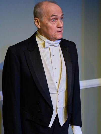 Elderly man in formal black tuxedo with white bow tie and gloves.